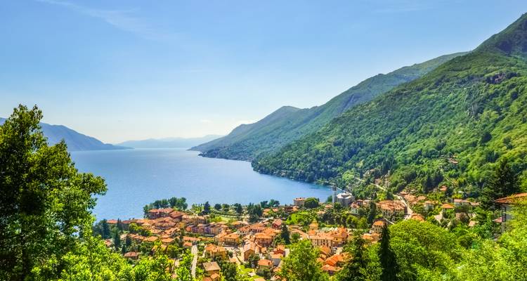 Vue panoramique sur un village au bord du lac entouré de collines boisées et d'une vaste étendue d'eau bleue qui s'étire au loin.