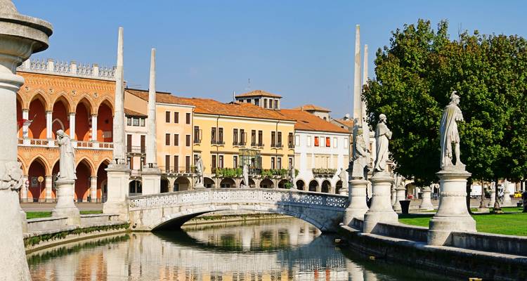 D'élégantes statues bordant le canal et le pont arqué du Prato della Valle de Padoue sous un ciel bleu dégagé.