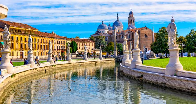 Canal serein à Padoue bordé de statues de pierre, bâtiments pastel et basilique à dôme sous un ciel bleu.