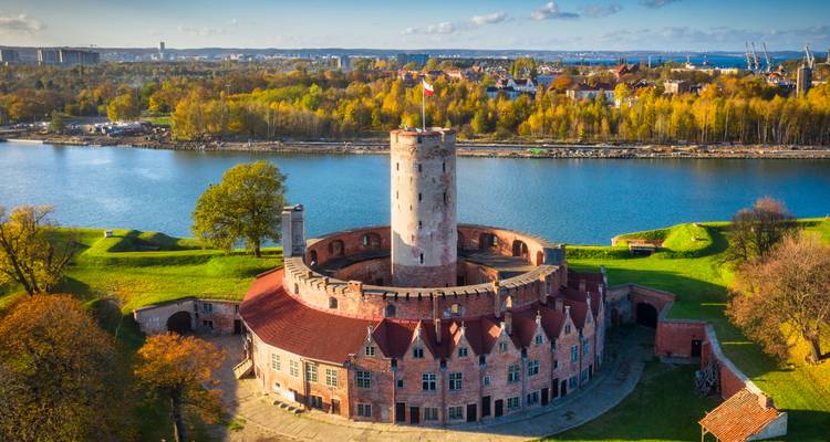 Vue aérienne d'une forteresse circulaire en brique entourée d'eau et de feuillage d'automne à Gdansk.