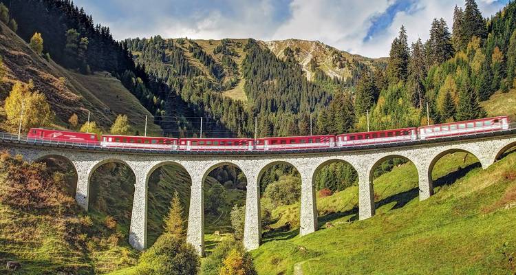 Un train panoramique rouge traverse un viaduc en pierre à arches au milieu de vallées alpines verdoyantes et de montagnes boisées.