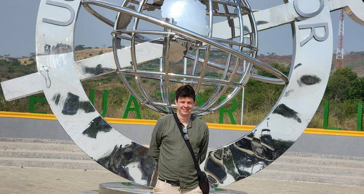 Un voyageur masculin pose devant un monument de globe équatorial brillant dans une place ouverte.