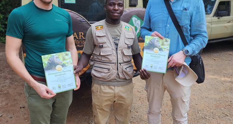 Deux touristes se tiennent avec un guide local qui présente des certificats de pistage de chimpanzés à côté d'un véhicule de safari.