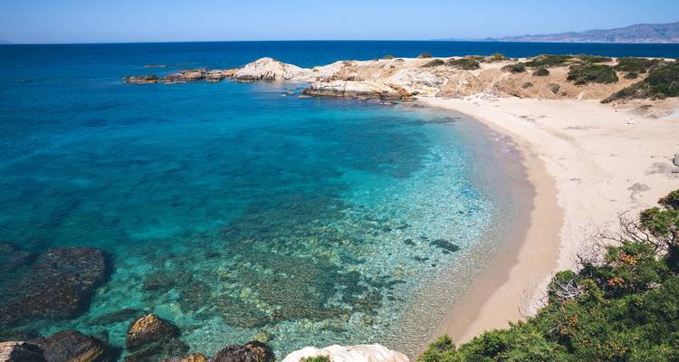 Plage en croissant isolée avec une eau turquoise claire et des promontoires rocheux par une journée ensoleillée.