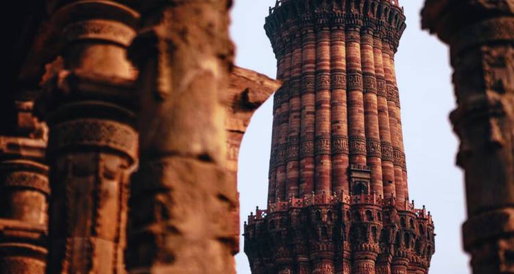 Close-up van de ingewikkeld gebeeldhouwde stenen toren Qutub Minar omlijst door oude zuilen