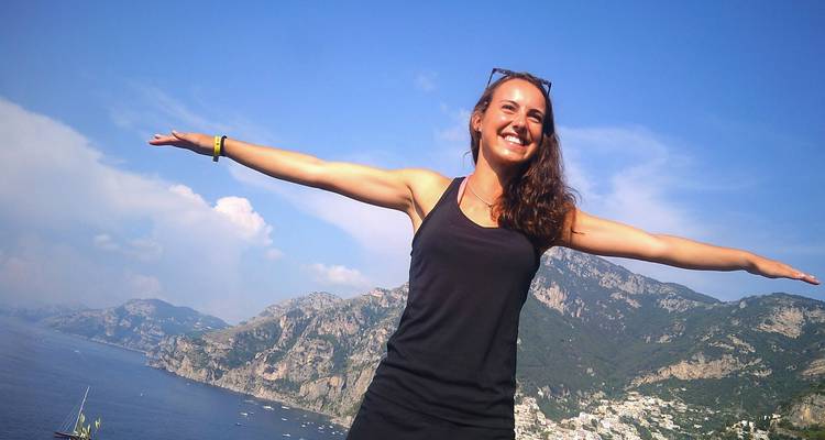 Jeune femme écarte les bras au sommet d'une falaise avec la côte amalfitaine et la mer en contrebas