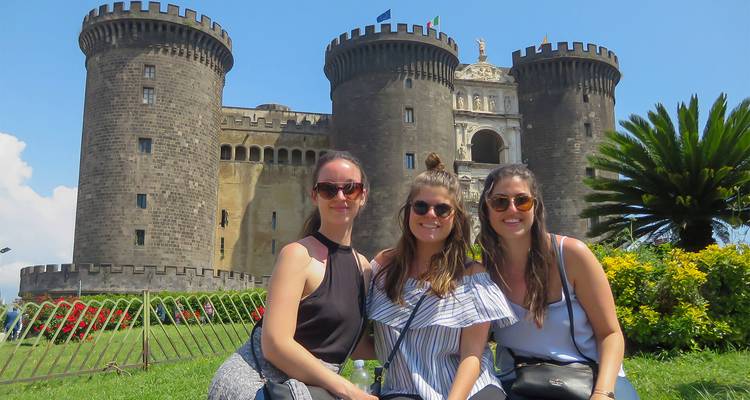 Trois voyageurs sont assis devant les tours médiévales du Castel Nuovo à Naples
