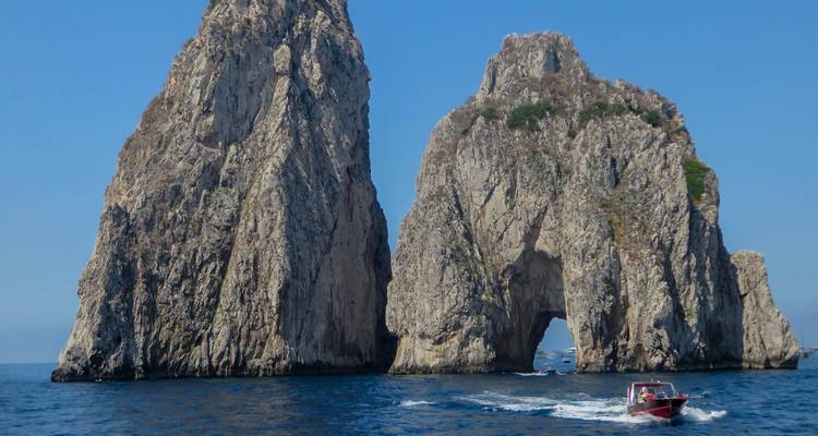 Un hors-bord file devant les iconiques rochers jumeaux Faraglioni au large de la côte de Capri