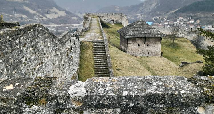 Verweerde stenen wallen en trappen van een oude heuveltop vesting die uitkijkt over een mistige vallei.