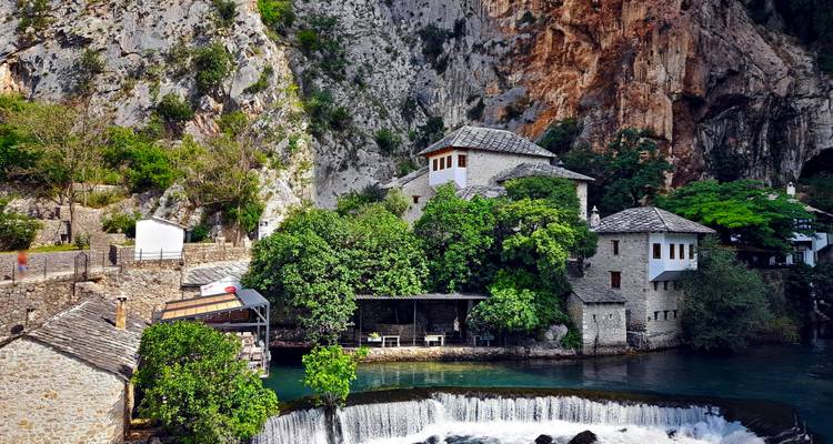 Blagaj Tekija klooster genesteld tegen een dramatische klif naast een blauwe rivier en waterval.