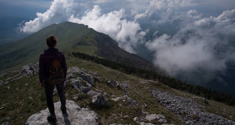 Een eenzame wandelaar staat op een rotsachtige bergkam en kijkt uit over met mist gevulde bergdalen onder dramatische wolken.