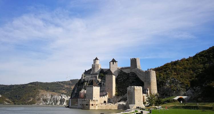 Een goed bewaard gebleven middeleeuwse stenen vesting verheft zich naast een brede rivier onder een heldere blauwe hemel.