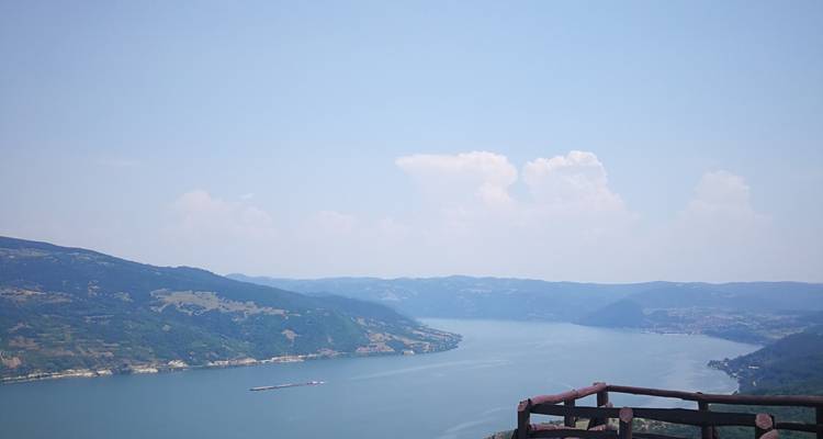 Een brede turquoise rivier kronkelt door verre heuvels gezien vanaf een houten uitkijkhek op een heldere dag.