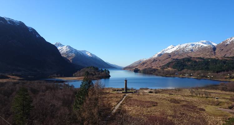 Le paisible Loch Shiel entouré de montagnes aux sommets enneigés avec le Monument de Glenfinnan sur sa rive.