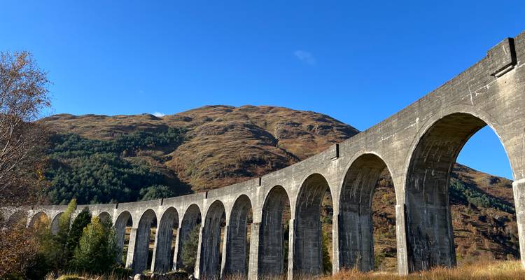 Les arches de pierre du viaduc de Glenfinnan s'élancent à travers une vallée boisée sous un ciel bleu clair.