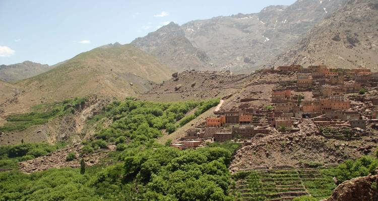 Ein terrassenförmiges Berberdorf schmiegt sich an grüne Hänge unterhalb der schroffen Gipfel des Hohen Atlas.