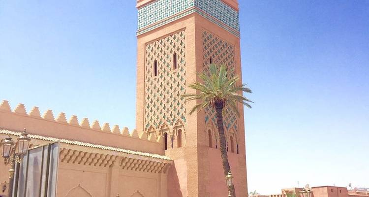 Ein hoher Minarett aus rosafarbenem Stein mit türkisfarbenen Kacheln erhebt sich gegen einen wolkenlosen blauen Himmel.