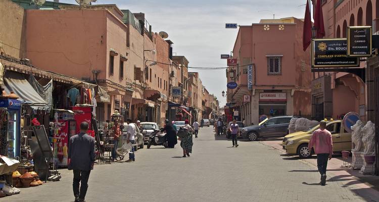Belebte enge Straße der Medina von Marrakesch, gesäumt von Geschäften, Rollern und Fußgängern.