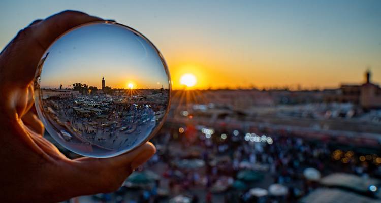 Kreativer Schuss von Marrakesch's belebtem Platz und Sonnenuntergang, eingefangen durch eine handgehaltene Glaskugel.