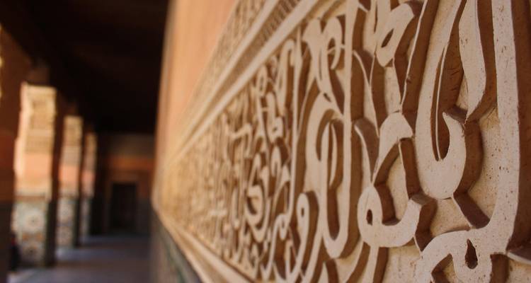 Nahaufnahme einer kunstvollen arabischen Steingravur entlang eines Korridors in einer historischen marokkanischen Madrasa.