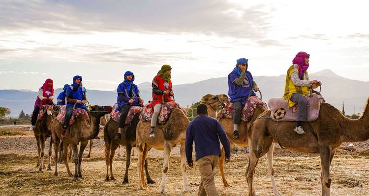 Touristen in heller Kleidung reiten auf Kamelen in einer Reihe über eine felsige Wüstenebene