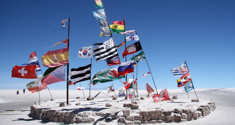Grappe de drapeaux internationaux flottant sur une base circulaire en pierre au milieu du salar d'Uyuni.