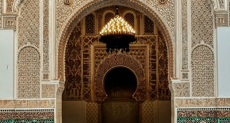 Detaillierter islamischer Torbogen und Kronleuchter im Inneren eines reich verzierten marokkanischen Palastes.