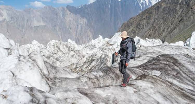 Randonneur avec bâtons navigue prudemment sur la glace dentelée du glacier sous un ciel dégagé et des sommets lointains.