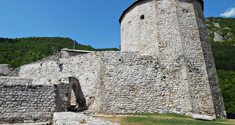 Stenen muren en een ronde toren van een oude heuveltopvesting onder een heldere blauwe hemel.