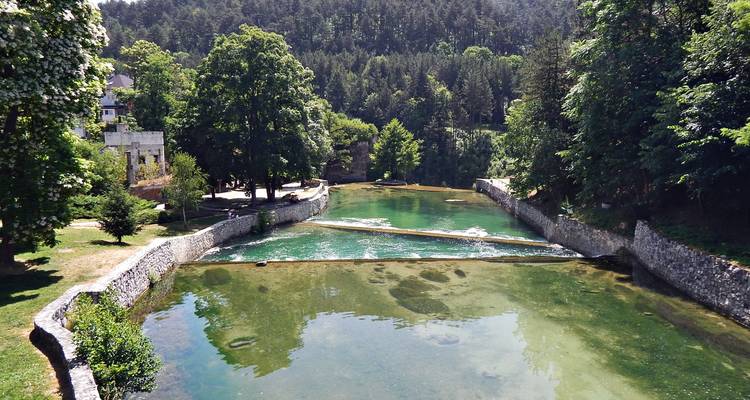 Heldere groene vijver en rivier omzoomd door stenen kademuren en beboste heuvels.