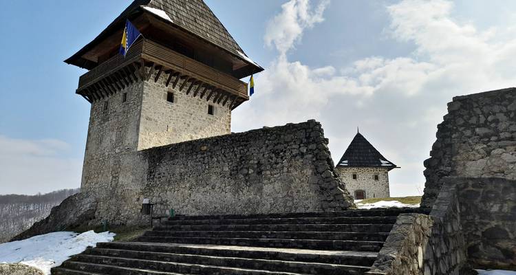 Tour de guet en pierre avec avant-toits en bois arborant des drapeaux bosniaques au-dessus de marches saupoudrées de neige.