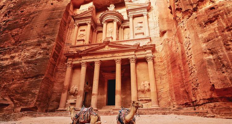 Verzierte Fassade von Petras Schatzkammer in warmes Licht getaucht mit farbenfroh gesattelten Kamelen in Ruhe.