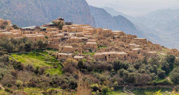 Steinruinen eines antiken Klippendorfes überblicken grüne Täler in Jordanien.