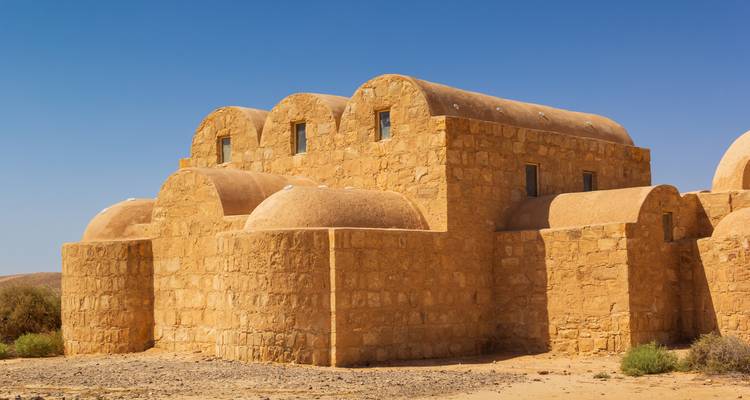 Das isolierte Wüstenschloss Qasr Amra steht unter einem klaren blauen jordanischen Himmel.