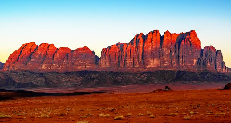 Rotes Sandsteinmassiv glüht im frühen Morgenlicht über dem Wüstenboden des Wadi Rum.