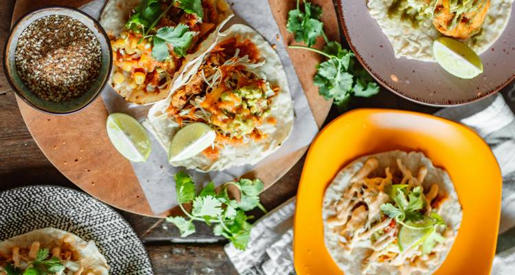 Vue de dessus de tacos mexicains colorés garnis de coriandre, quartiers de citron vert et garnitures sur une table rustique.