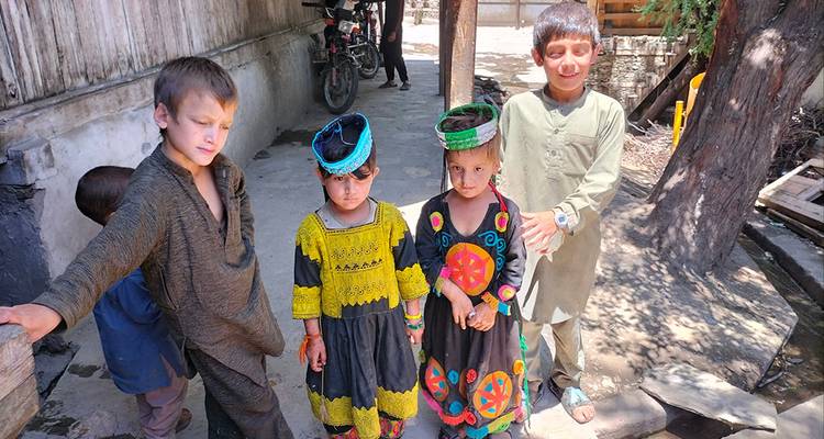 Grupo de niños kalash con ropa colorida parados junto a una calle arbolada.