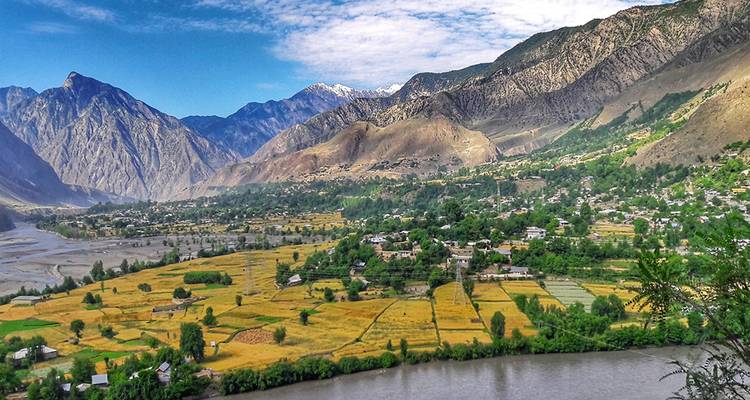 Valle agrícola exuberante bordeado por montañas escarpadas y un río serpenteante.