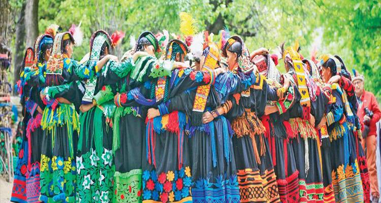 Gran círculo de mujeres Kalash bailando con vestidos multicolores en un claro del bosque.