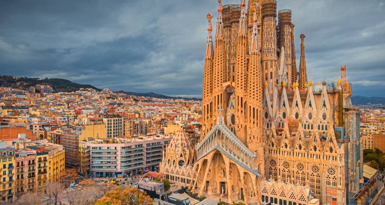 Vue emblématique de la Sagrada Família s'élevant au-dessus du paysage urbain de Barcelone sous un ciel dramatique.
