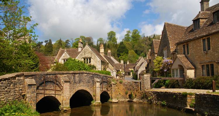 Pueblo quintaesencial de los Cotswolds con casas de piedra, puente de piedra arqueado y arroyo tranquilo en un día de primavera.