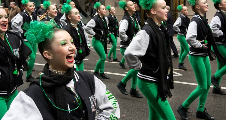 Bailarines alegres en trajes verdes marchando durante un desfile del Día de San Patricio.