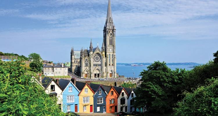 Rangée emblématique de maisons colorées à flanc de colline menant à la cathédrale Saint-Colman surplombant le port de Cobh et la mer au loin.