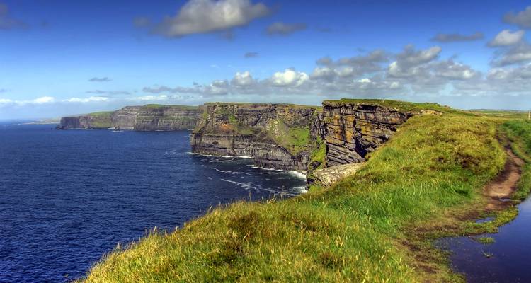 Steile Klippen erheben sich aus dem Atlantik an den berühmten Cliffs of Moher unter blauem Himmel.