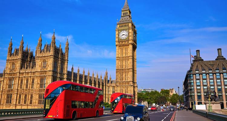 Big Ben et les Chambres du Parlement se dressent au-dessus du pont de Westminster tandis que des bus rouges à impériale passent.