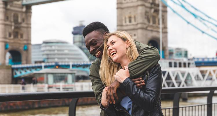 Couple souriant qui s'enlace avec le Tower Bridge de Londres et la Tamise flous en arrière-plan.
