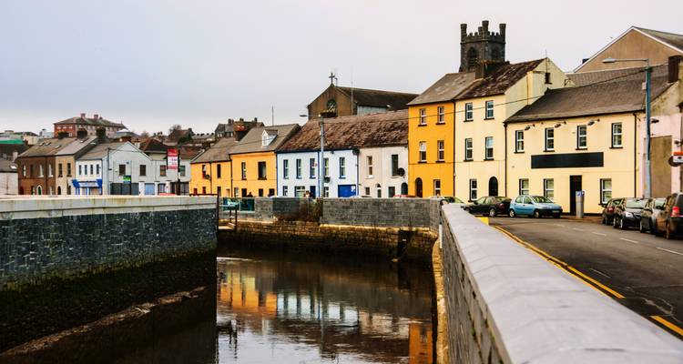 Colorful riverside houses and church tower reflected in calm water on an overcast Irish morning.