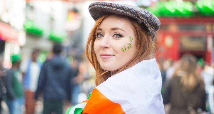 Young woman wrapped in Irish flag with shamrock face paint smiles over shoulder during street festival