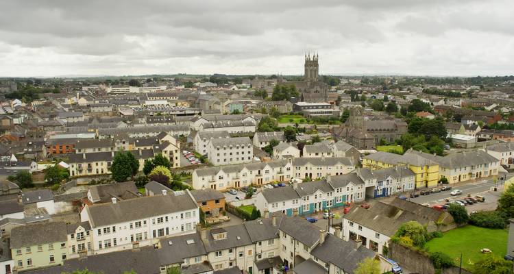 Panorama aéreo nublado de la ciudad de Kilkenny salpicada de campanarios de iglesias, techos grises y casas agrupadas que se extienden hasta el horizonte.