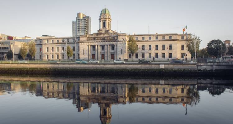 Ayuntamiento neoclásico de la ciudad de Cork y torres modernas reflejadas en el río tranquilo a la luz del amanecer.